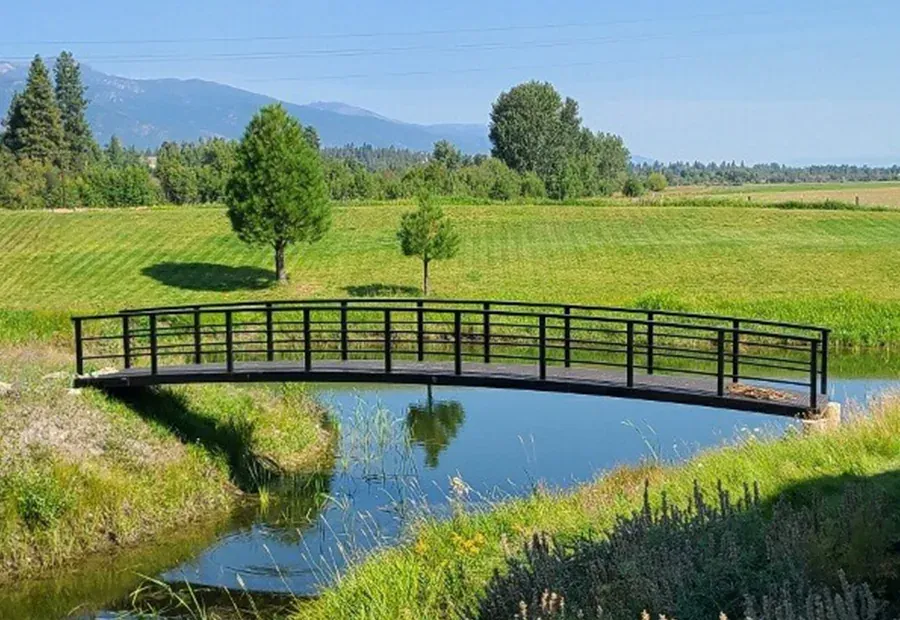 Arched modular pedestrian bridge with black steel rails and timber deck over a canal.