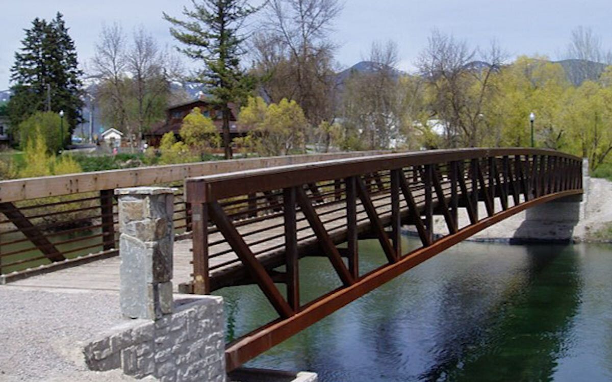 Curved single-span footbridge with brown steel rails and wood deck over water.