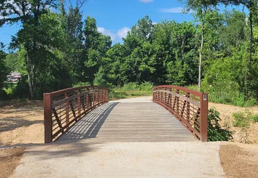 Arched weathering-steel pedestrian bridge with wood deck on a park trail.