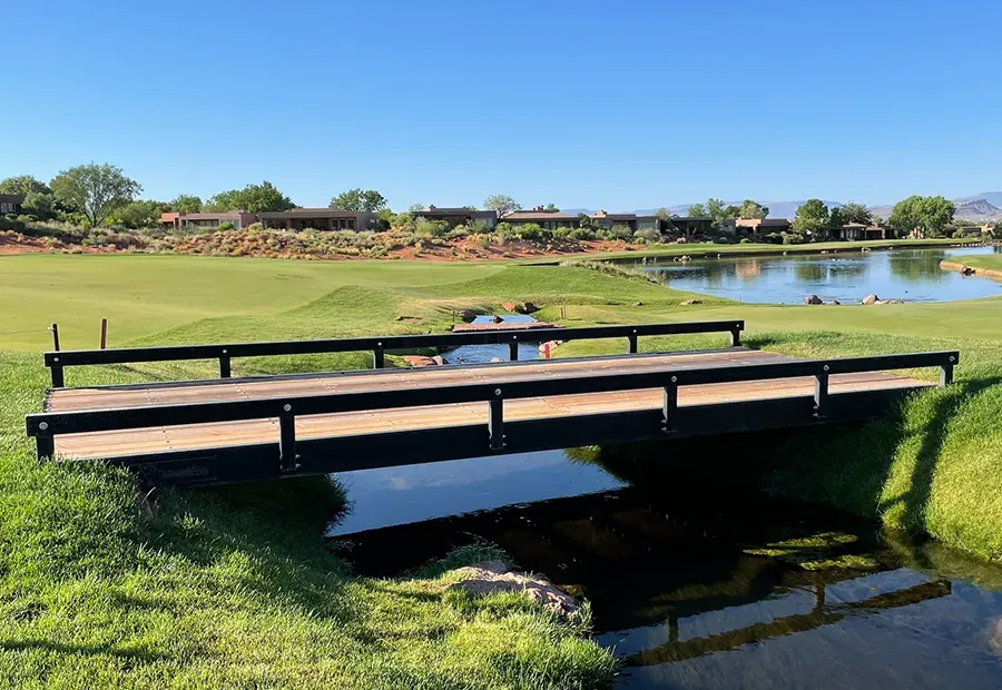 Modular steel-rail, timber-deck footbridge over a golf course creek.